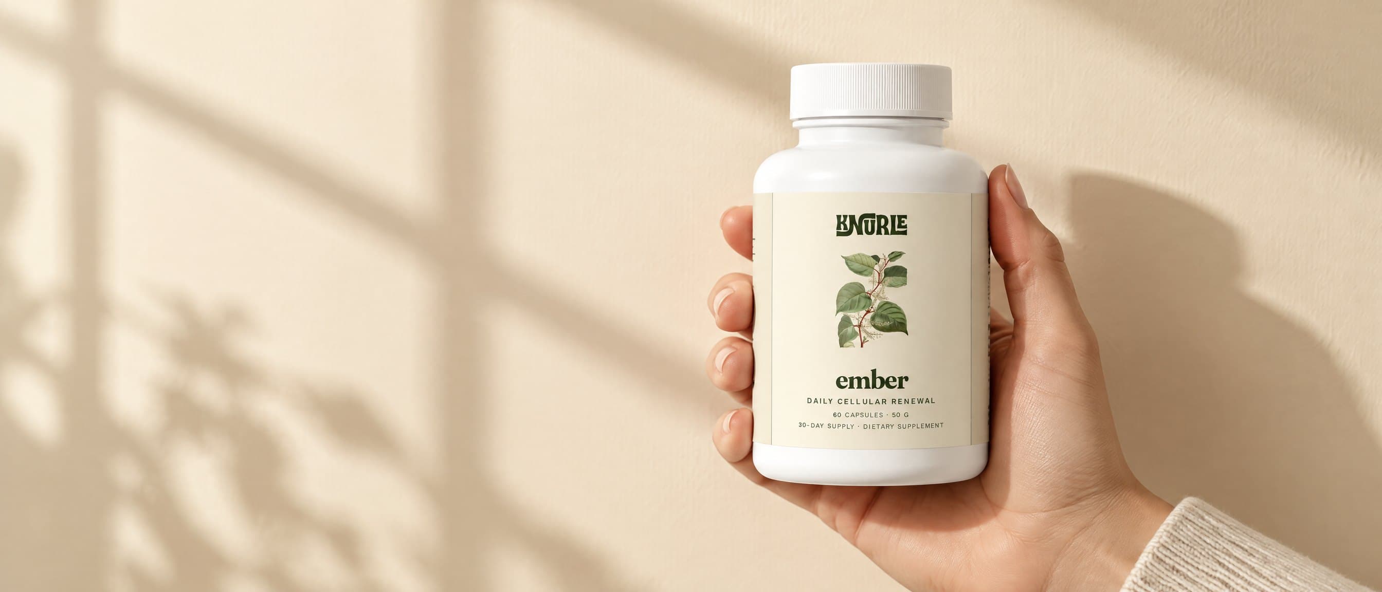 A hand holding a bottle of Ember against a cream wall crossed by window shadows