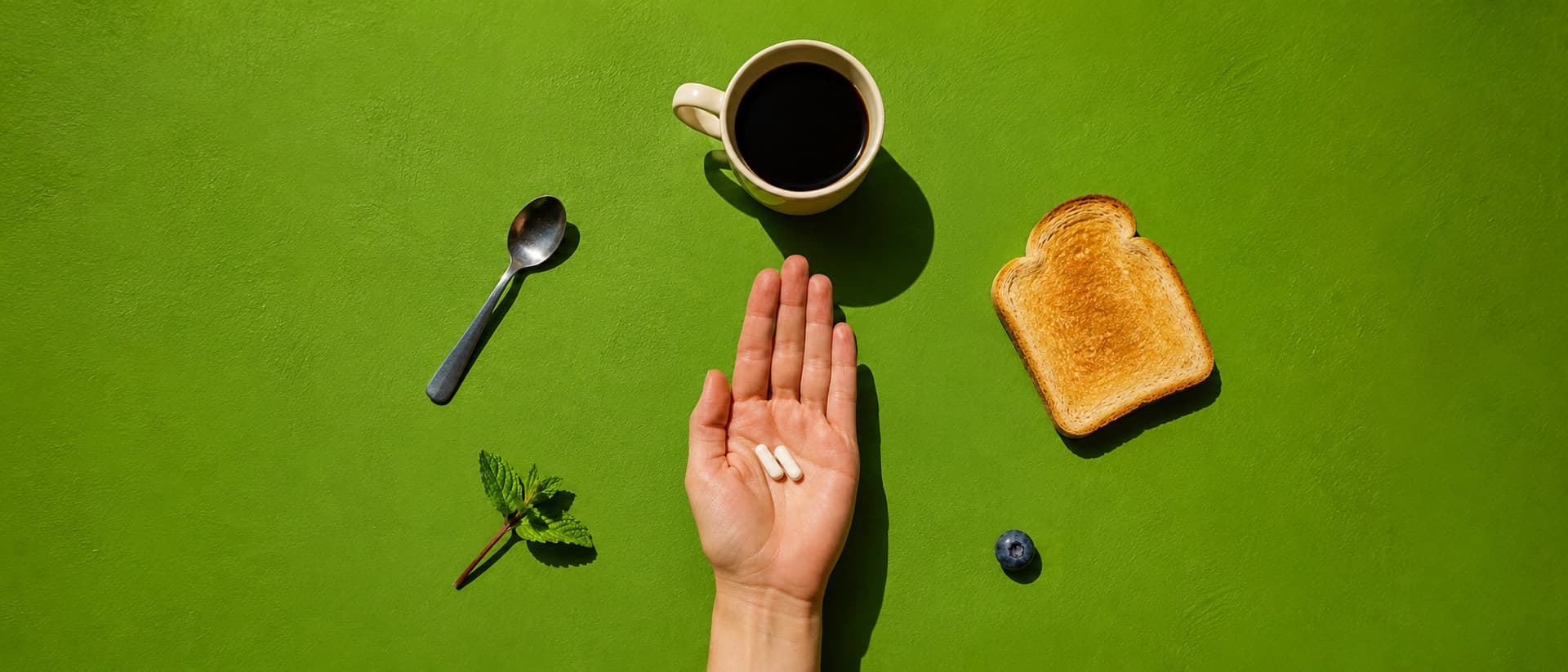 Two capsules in an open palm on a green table, laid out with breakfast things
